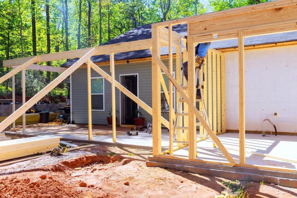 Workers install wooden beams for home extension in wooded area during trusses frame